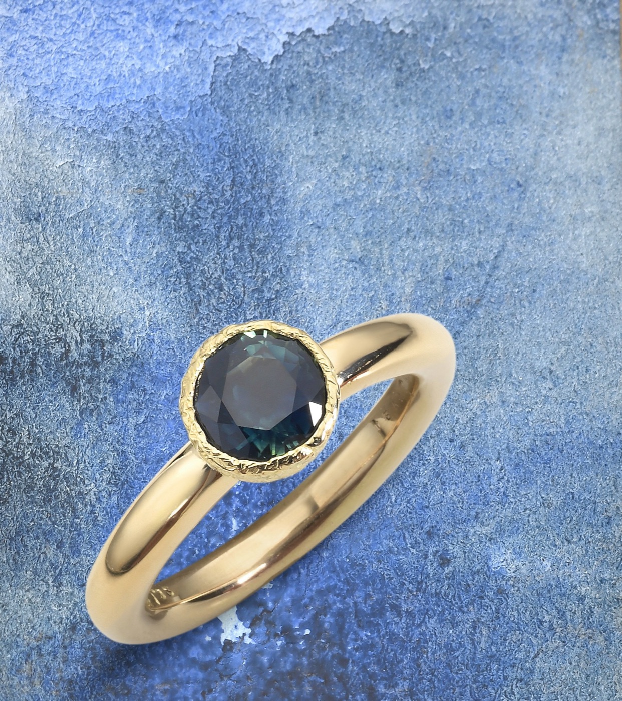 an 18k gold ring set with a teal sapphire